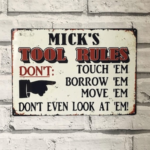 May include: A rectangular metal sign with the text "MICK'S TOOL RULES" in red and black lettering. The sign includes the phrases "DON'T: TOUCH 'EM, BORROW 'EM, MOVE 'EM, DON'T EVEN LOOK AT 'EM!" and a pointing hand graphic.
