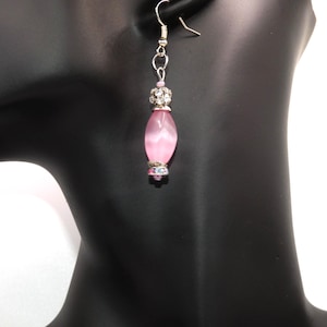 May include: Pink oval-shaped dangle earrings with a silver chain and a clear rhinestone cluster at the top.