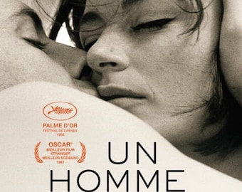 May include: A black and white poster for the French film "Un Homme et Une Femme" (A Man and a Woman). The poster features a close-up of a couple embracing. The title of the film is written in large, bold letters. The poster also includes the film's credits, including the director, Claude Lelouch, and the stars, Anouk Aimée and Jean-Louis Trintignant.