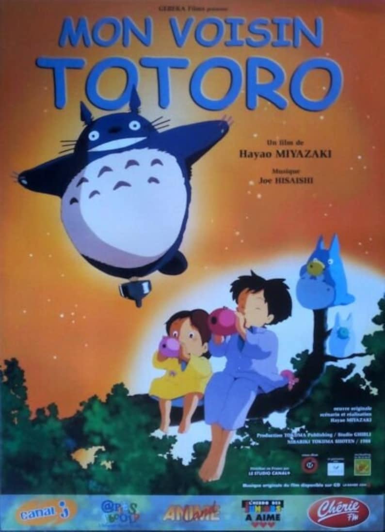 K&ouml;nnte beinhalten: Ein Filmplakat f&uuml;r den Film "Mein Nachbar Totoro" mit einer gro&szlig;en, flauschigen, grau-wei&szlig;en Kreatur mit gro&szlig;en Ohren und einem breiten L&auml;cheln. Die Kreatur fliegt in der Luft mit einem kleinen, runden Objekt, das an ihrem Bauch befestigt ist. Zwei Kinder sitzen im Vordergrund auf einem Baumzweig, &uuml;ber ihnen sitzt eine kleinere, blaue Kreatur auf einem Ast. Das Plakat ist auf Franz&ouml;sisch und zeigt den Titel "Mon Voisin Totoro" sowie die Namen des Regisseurs, Hayao Miyazaki, und des Komponisten, Joe Hisaishi.