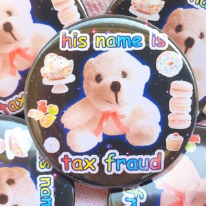 May include: A black button with a white teddy bear wearing a pink ribbon. The button has a black background with colorful text that reads "his name is tax fraud". The button is surrounded by other buttons with various designs.