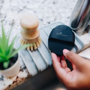 May include: A black silicone facial cleansing brush with the text "EFFILOGIC" on it. The brush is sitting on a gray silicone dish drainer.