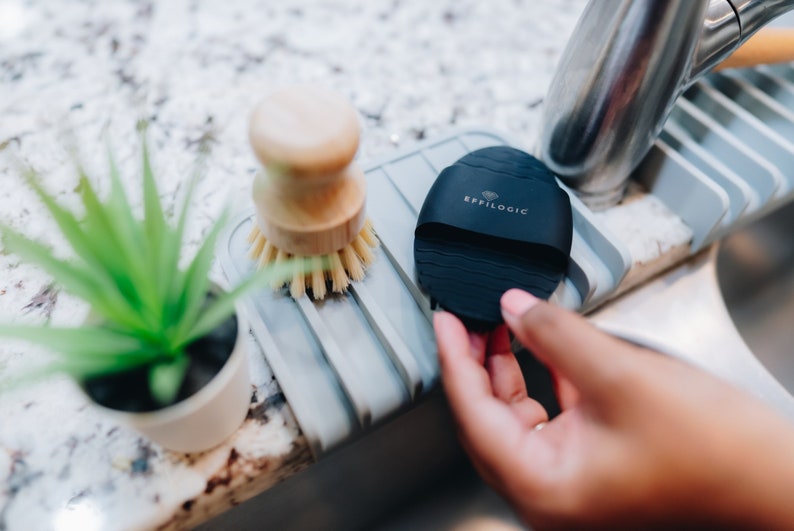 May include: A black silicone facial cleansing brush with the text "EFFILOGIC" on it. The brush is sitting on a gray silicone dish drainer.