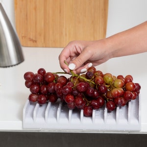 K&ouml;nnte beinhalten: Ein grauer Silikon-Obst- und Gem&uuml;seabtropfgestell mit roten Trauben darauf. Das Gestell hat mehrere Rippen, damit das Wasser abtropfen kann.