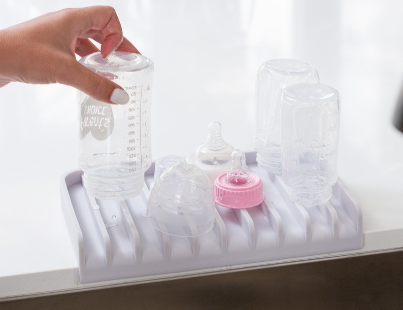 K&ouml;nnte beinhalten: Ein wei&szlig;er Babyflaschen-Abtropfst&auml;nder aus Kunststoff mit sechs durchsichtigen Glas-Babyflaschen und zwei durchsichtigen Plastik-Saugern. Eine Flasche tr&auml;gt das Etikett "Choice Organics".