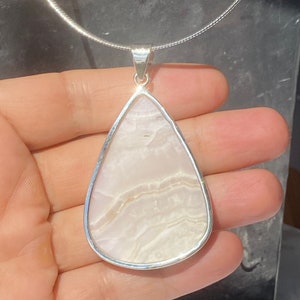 May include: A teardrop-shaped pendant with a white agate stone set in a silver frame. The pendant is hanging from a silver chain.