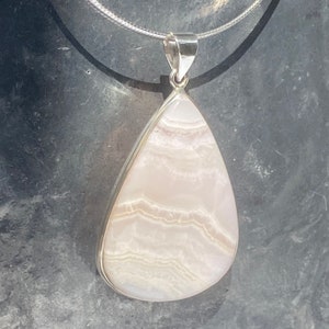 May include: A teardrop-shaped pendant with a white and pink agate stone set in sterling silver.
