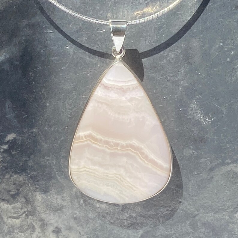 May include: A teardrop-shaped pendant with a white and pink agate stone set in sterling silver.
