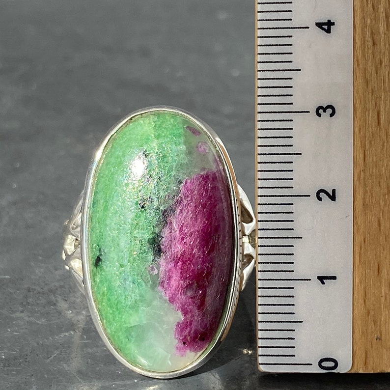 K&ouml;nnte beinhalten: Ein silberner Ring mit einem ovalen, gr&uuml;n-rosa Edelstein. Der Ring liegt neben einem Lineal, das zeigt, dass der Stein etwa 2,5 cm lang ist.