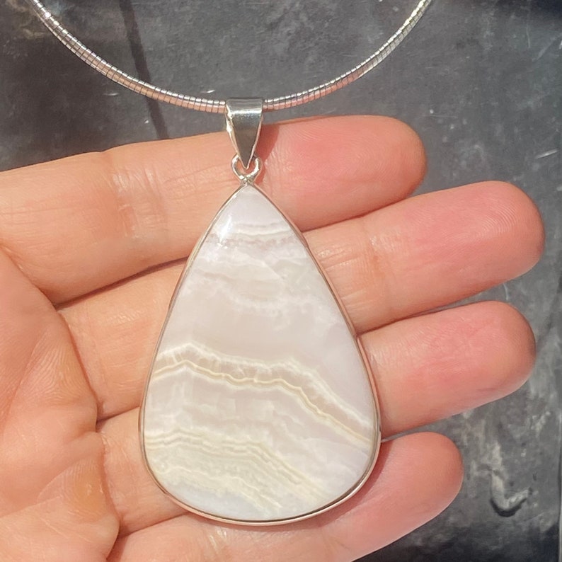 May include: A white and silver teardrop-shaped pendant necklace with a white agate stone. The stone has a layered, striated pattern.