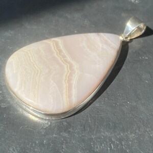 May include: A white agate pendant with a silver setting. The agate has a layered, striped pattern.