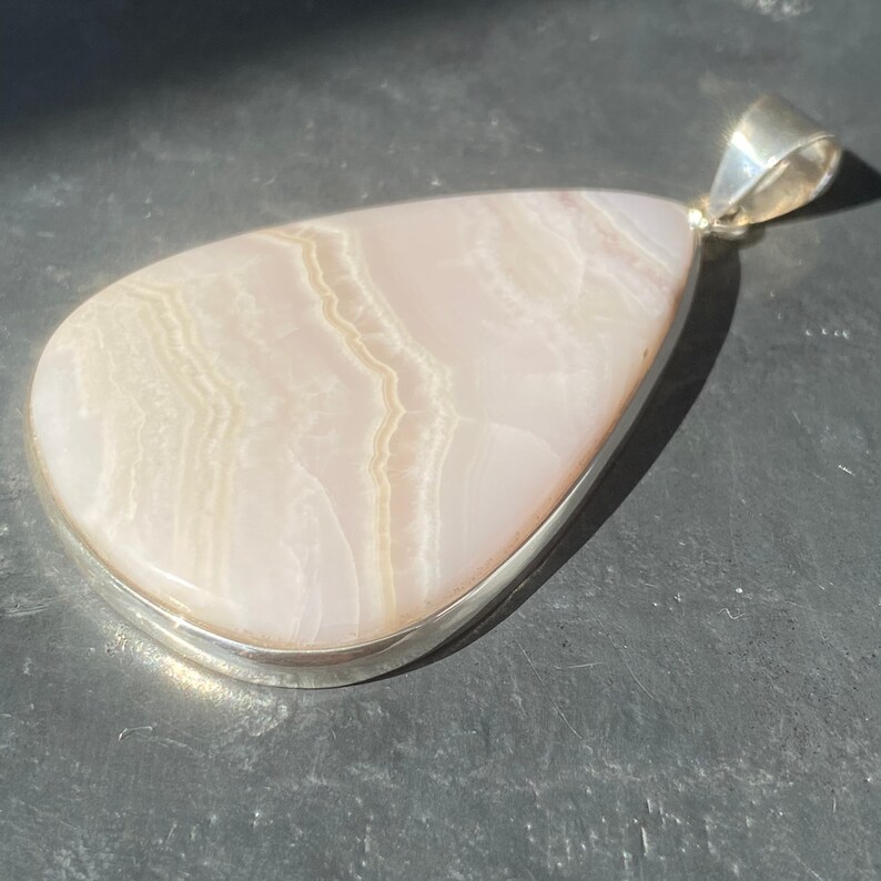 May include: A white agate pendant with a silver setting. The agate has a layered, striped pattern.
