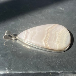 May include: A teardrop-shaped pendant with a silver setting and a pink and white agate stone.