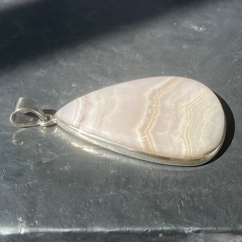 May include: A teardrop-shaped pendant with a silver setting and a pink and white agate stone.