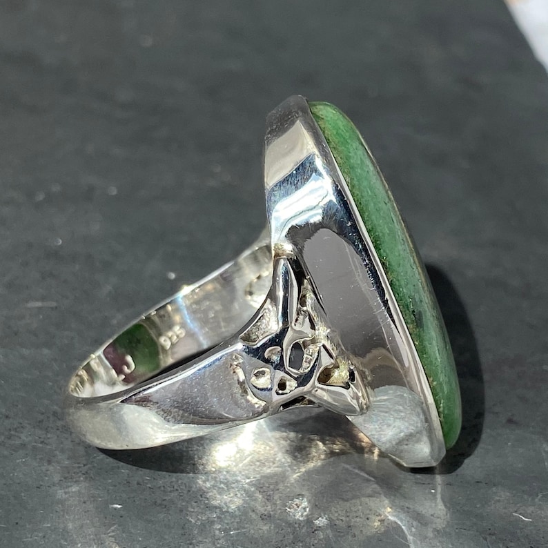 K&ouml;nnte beinhalten: Ein silberner Ring mit einem gr&uuml;nen ovalen Edelstein, der in einem filigranen Design gefasst ist.