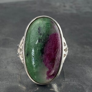 K&ouml;nnte beinhalten: Ein silberner Ring mit einem ovalen, gr&uuml;n-rosa Edelstein. Der Edelstein hat ein einzigartiges Muster aus Gr&uuml;n und Rosa.