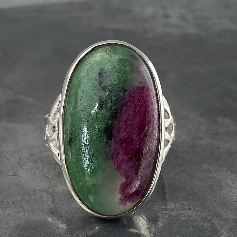 K&ouml;nnte beinhalten: Ein silberner Ring mit einem ovalen, gr&uuml;n-rosa Edelstein. Der Edelstein hat ein einzigartiges Muster aus Gr&uuml;n und Rosa.