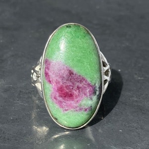 May include: A silver ring featuring a large oval green and pink gemstone. The gemstone has a swirling pattern of green and pink.