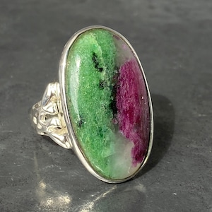 K&ouml;nnte beinhalten: Ein silberner Ring mit einem gro&szlig;en ovalen gr&uuml;n-rosa Edelstein. Der Edelstein hat ein geflecktes Muster aus Gr&uuml;n, Rosa und Wei&szlig;.