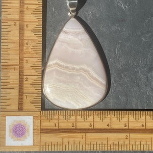 May include: A teardrop-shaped pendant made of white and pink banded agate, set in sterling silver. The pendant measures approximately 2 inches in length.