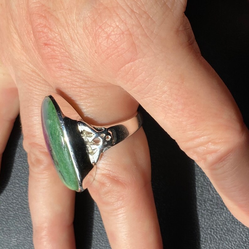 K&ouml;nnte beinhalten: Ein silberner Ring mit einem ovalen, gr&uuml;n-rosa Edelstein. Der Ring hat ein filigranes Design.