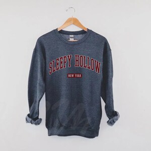 Może przedstawiać: Szara bluza z nadrukiem "SLEEPY HOLLOW NEW YORK" w kolorze bordowym.