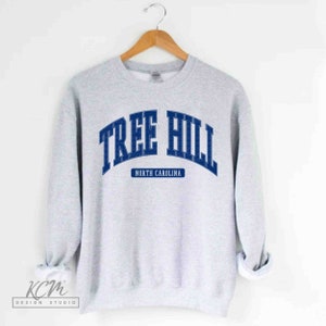 Pu&ograve; includere: Felpa grigia con una grafica blu che dice "Tree Hill North Carolina".