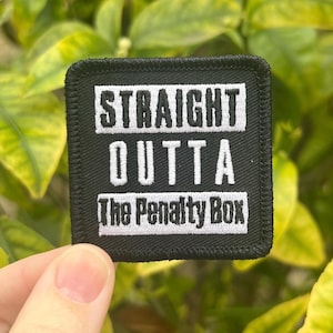 Op de afbeelding: Zwarte geborduurde patch met witte tekst die "STRAIGHT OUTTA The Penalty Box" luidt.