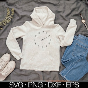 May include: A light grey hooded sweatshirt with a clock face design on the front. The clock face has black hands and black numbers. The sweatshirt is lying on a grey fabric background.