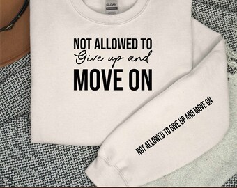 Może przedstawiać: Biała bluza z nadrukiem "NOT ALLOWED TO Give up and MOVE ON" z przodu i tym samym nadrukiem na rękawie.