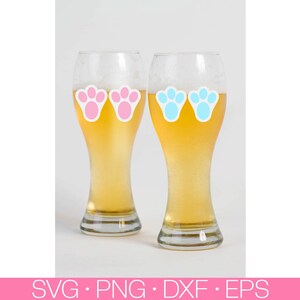 May include: Two clear glass beer mugs with pink and blue bunny paw prints on them. The mugs are filled with a light yellow beer.