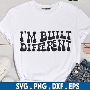 Pode incluir: Camiseta branca com texto preto que diz "I'm Built Different" em uma fonte retrô e ondulada.