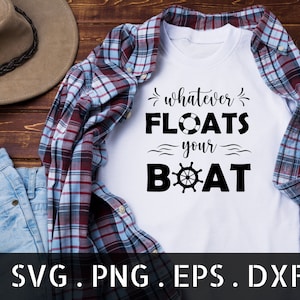 以下が含まれることがあります： 白いTシャツに、黒いグラフィックで「whatever floats your boat」と書いてあり、船の舵のデザインが施されています。Tシャツは、格子柄の布と木製の表面の上に置かれています。