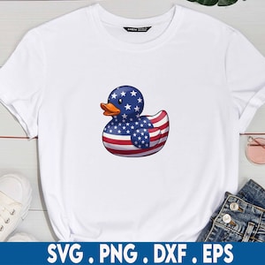 Puede incluir: Una camiseta blanca con un dise&ntilde;o de pato de goma. El pato est&aacute; decorado con la bandera estadounidense.