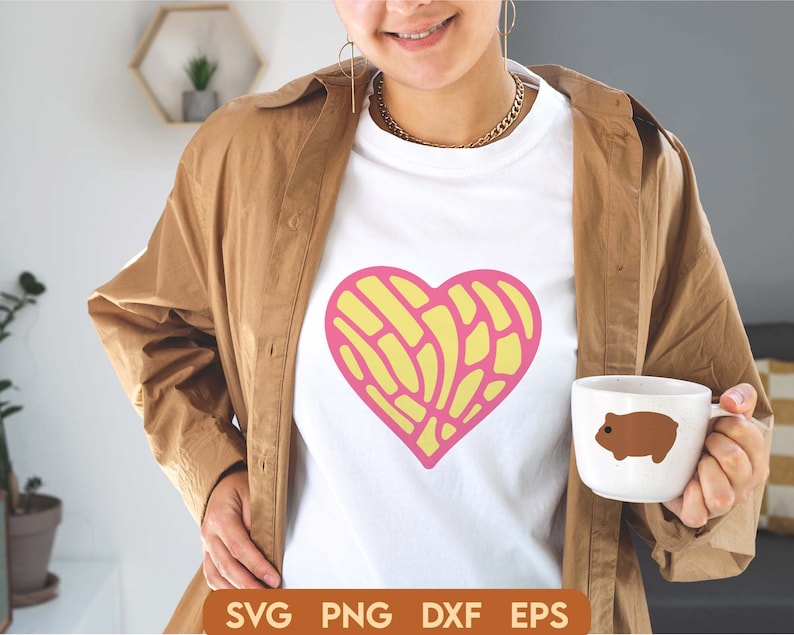 May include: A white t-shirt with a pink and yellow heart design. The heart is made up of a pattern of lines and swirls. The t-shirt is being worn by a person with a brown jacket.