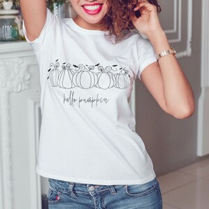May include: White t-shirt with a black line drawing of pumpkins and bats. The text "hello pumpkin" is written below the pumpkins.