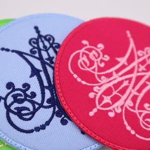 May include: Close-up of three round fabric patches in shades of green, light blue, and red. Each patch features an embroidered ornate design in a contrasting color. The patches have a stitched border.