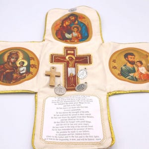 May include: Cream-colored religious item with gold trim, featuring illustrations of religious figures and a central crucifix. Includes a wooden cross, two medals, and printed text.