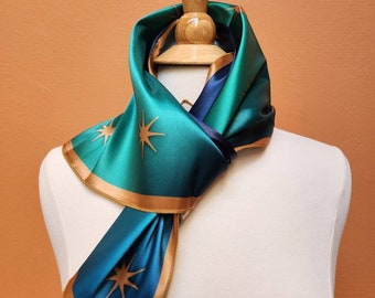 May include: A green and blue silk scarf with gold trim and a star pattern. The scarf is tied around a wooden mannequin's neck.