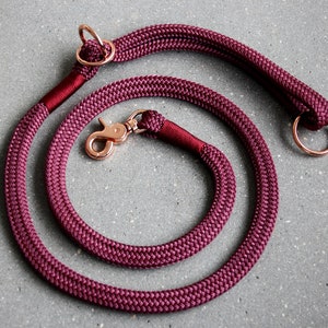 May include: Burgundy red rope dog lead with rose gold hardware, including a clip and two D-rings.