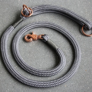 May include: A gray rope dog leash with a rose gold clip and two rose gold rings. The leash is made of a braided rope with a textured pattern.