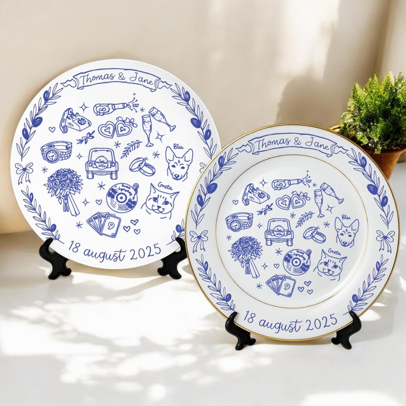 May include: Two white ceramic plates featuring blue line art illustrations of a wedding bouquet, car, rings, champagne, and pets named Blu and Greta. The text reads Thomas & Jane and 18 august 2025. Each plate is displayed on a black plastic stand.