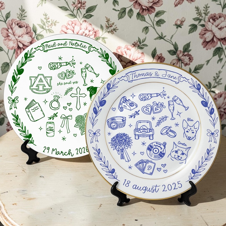 May include: Two white ceramic decorative plates featuring custom illustrations. The left plate has green ink with the text 'Reid and Natalie' and '29 March 2026'. The right plate has blue ink with the text 'Thomas & Jane' and '18 August 2025'.