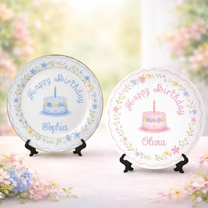 May include: Two decorative birthday plates with cake illustrations. One plate has a blue floral border, a blue cake, and the name "Sophia." The other plate has a pink floral border, a pink cake, and the name "Olivia." Both plates have "Happy Birthday" text.