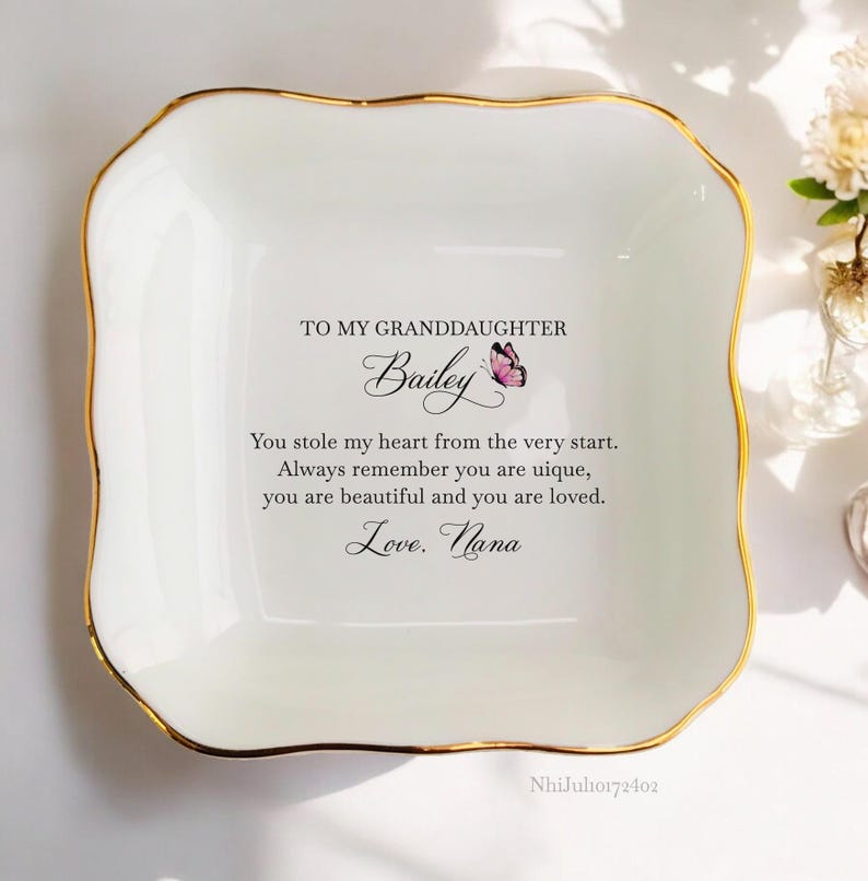Puede incluir: Un plato de porcelana blanca con borde dorado para guardar peque&ntilde;os objetos. El plato tiene un mensaje que dice: "A mi nieta Bailey Me robaste el coraz&oacute;n desde el principio. Recuerda siempre que eres &uacute;nica, eres hermosa y eres amada. Con amor. Abuela"