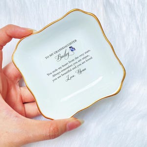 Puede incluir: Plato de cer&aacute;mica blanca para joyas con borde dorado y un mensaje que dice "To my granddaughter Bailey You stole my heart from the very start. Always remember you are unique, you are beautiful and you are loved. Love. Nana"