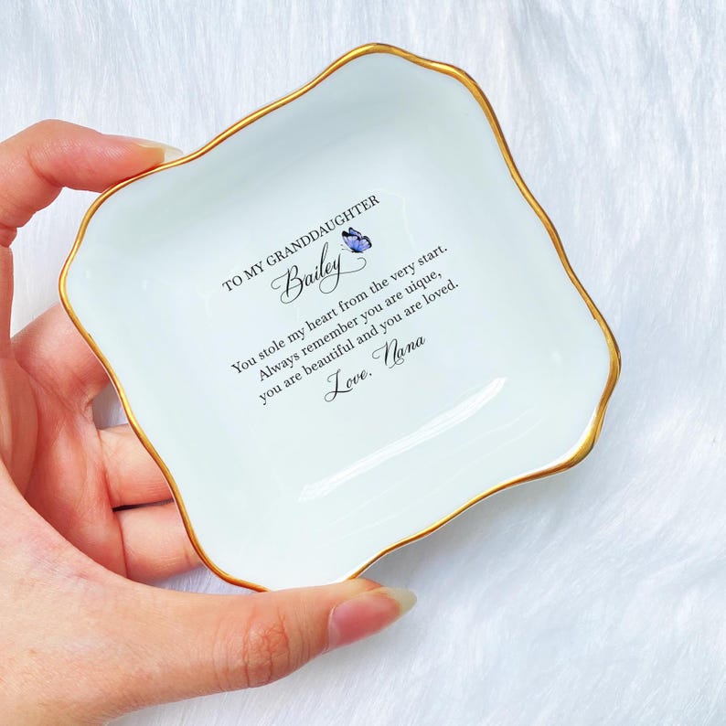 Puede incluir: Plato de cer&aacute;mica blanca para joyas con borde dorado y un mensaje que dice "To my granddaughter Bailey You stole my heart from the very start. Always remember you are unique, you are beautiful and you are loved. Love. Nana"