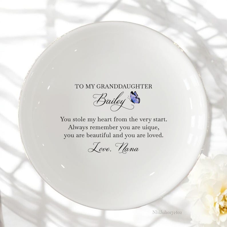 Puede incluir: Plato de cer&aacute;mica blanca para alhajas con una mariposa azul y el texto "TO MY GRANDDAUGHTER Bailey You stole my heart from the very start. Always remember you are unique, you are beautiful and you are loved. Love. Nana"