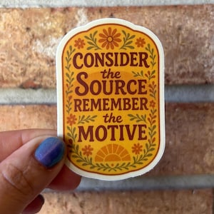 May include: A sticker with a cream-colored background and a decorative border. The sticker features the text "CONSIDER the SOURCE REMEMBER the MOTIVE" in a mix of orange and brown colors. Floral and sunburst designs are also included.
