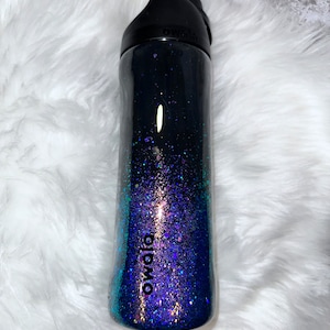 Può includere: Una bottiglia d'acqua nera e turchese con glitter con la scritta "owala" stampata sul lato.